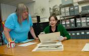 Area is a photo of the Alexander Architectural Archives area.  Two women admire some documents at a table.