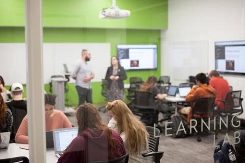 students working in a glassed-in room with a green back wall