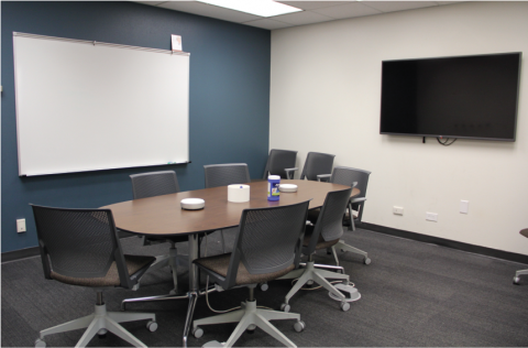 an empty conference room with desk, seating, and whiteboard