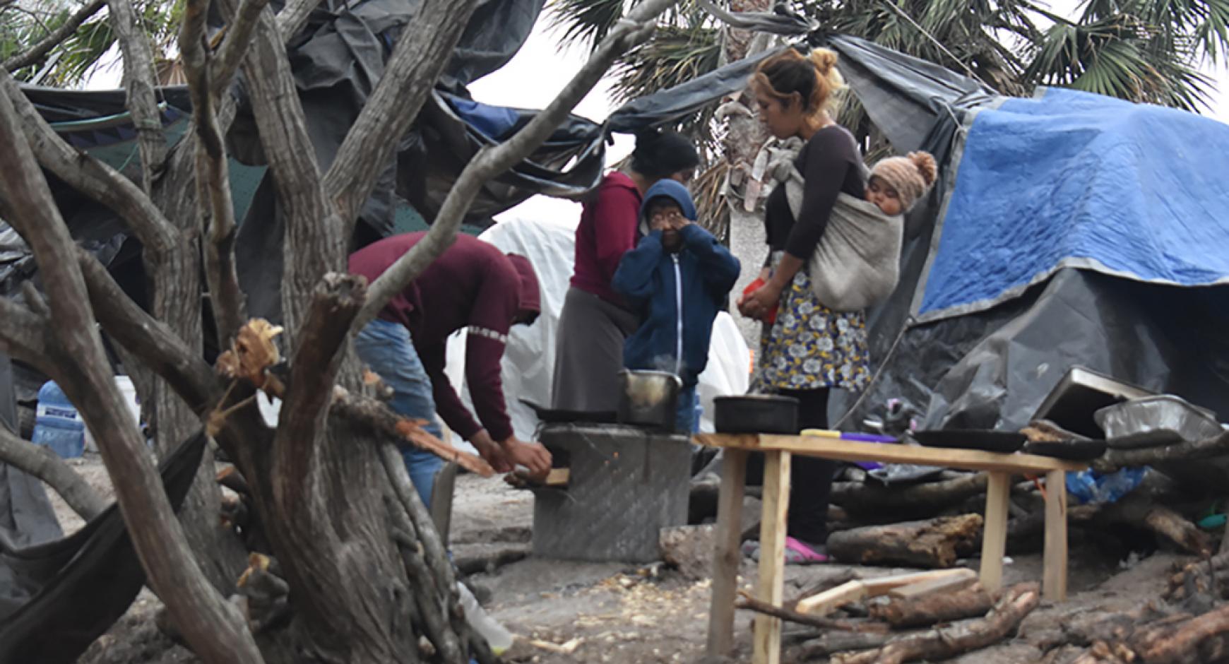 woman with child in refugee camp surrounded by tents and working men