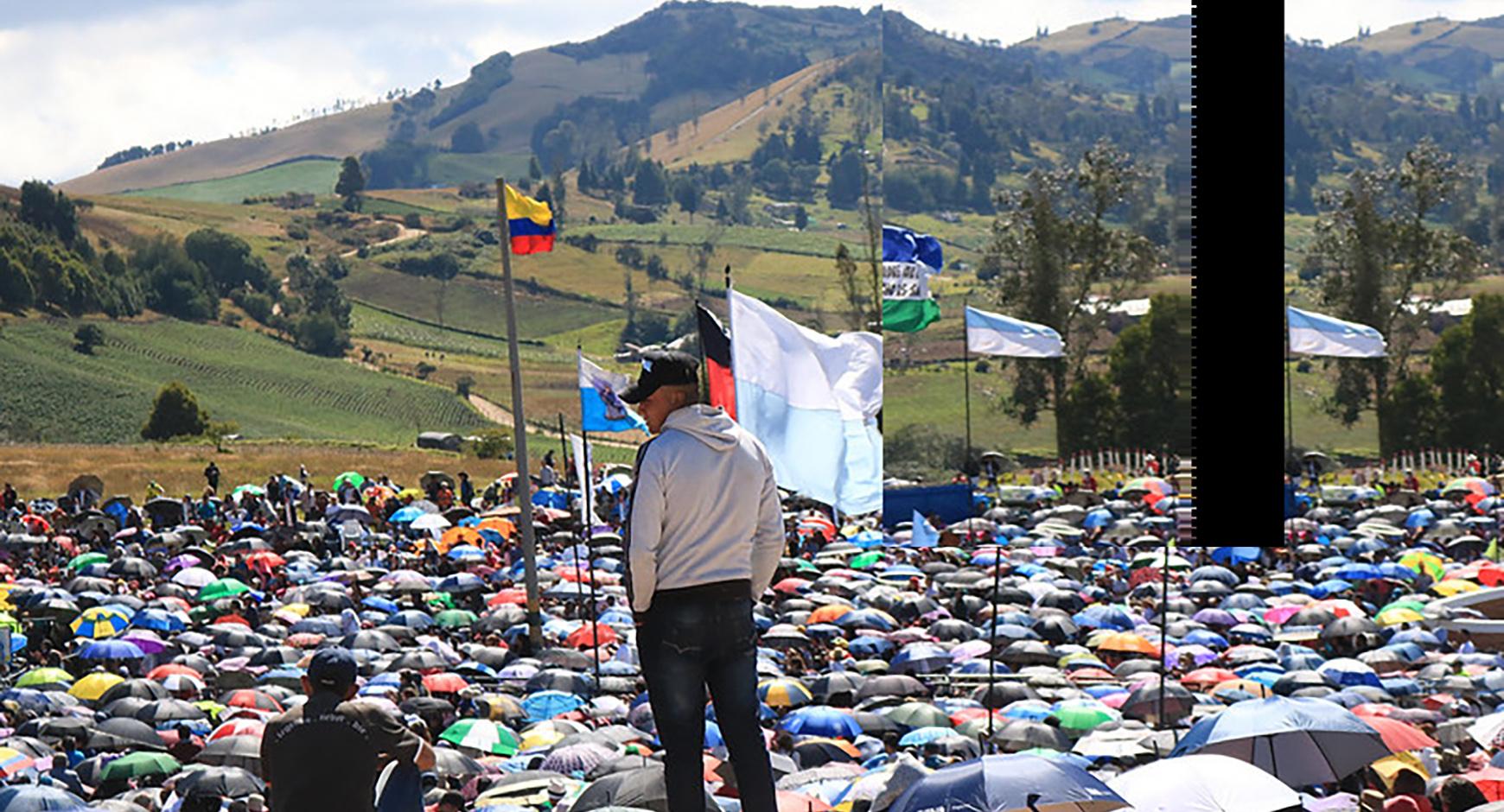 Man standing above field of umbrellas at rally. Feature image taken in Boyacá, Colombia, by Sofia Mock.