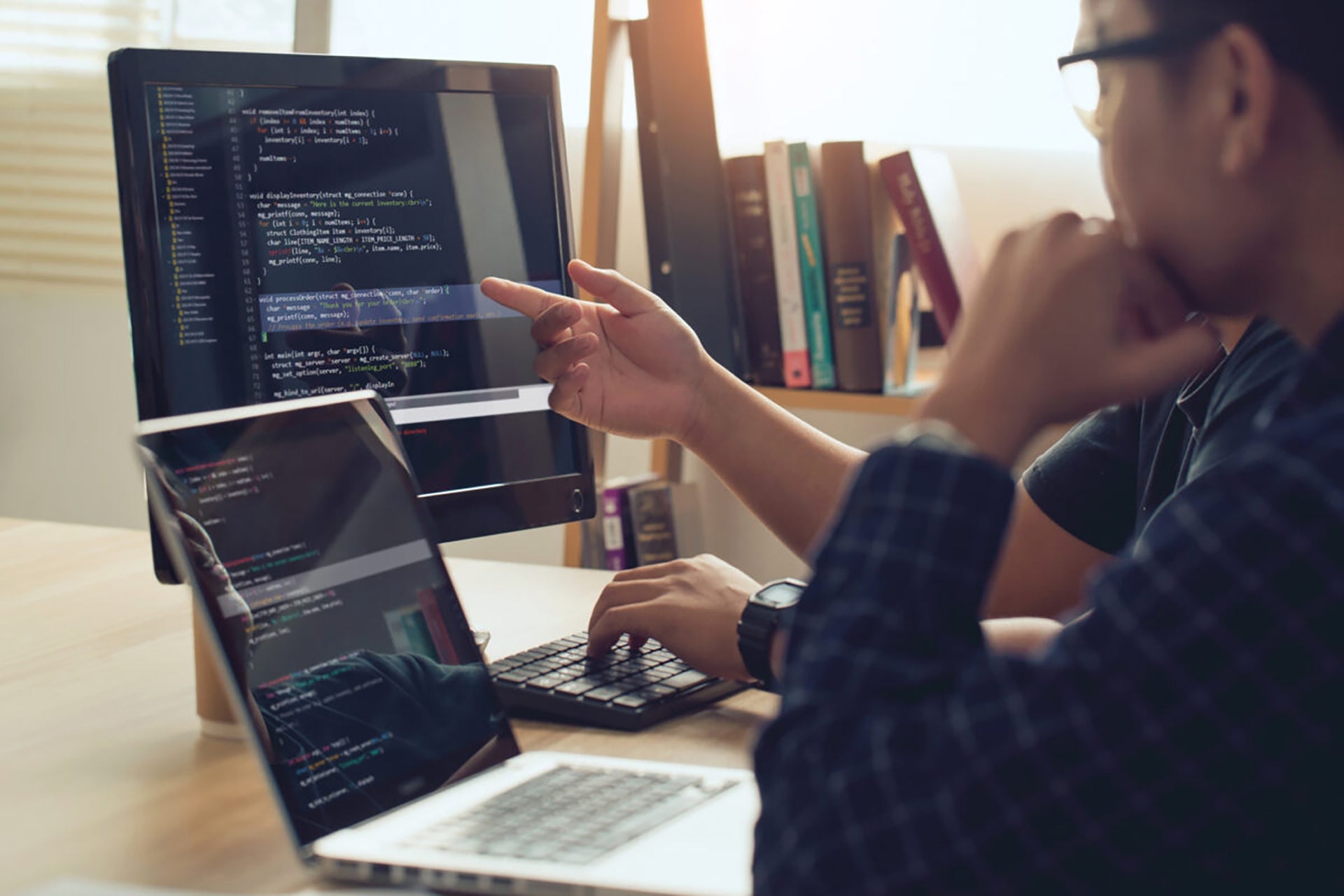 People sitting at a desk looking at desktop and laptop screens with formulas on them.