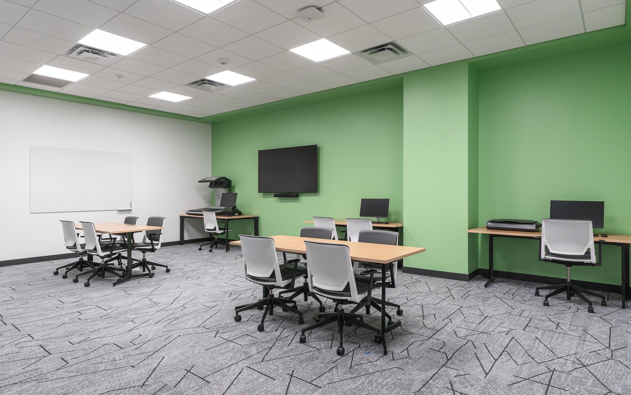 a series of computer desks and tables against a green wall