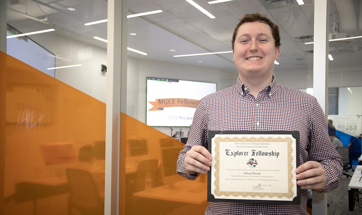 Ethan Plevak holding award certificate in front of computer lab window