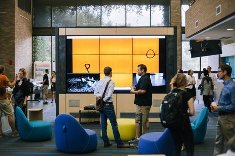 Gathering of individuals in front of a large wall-sized video screen