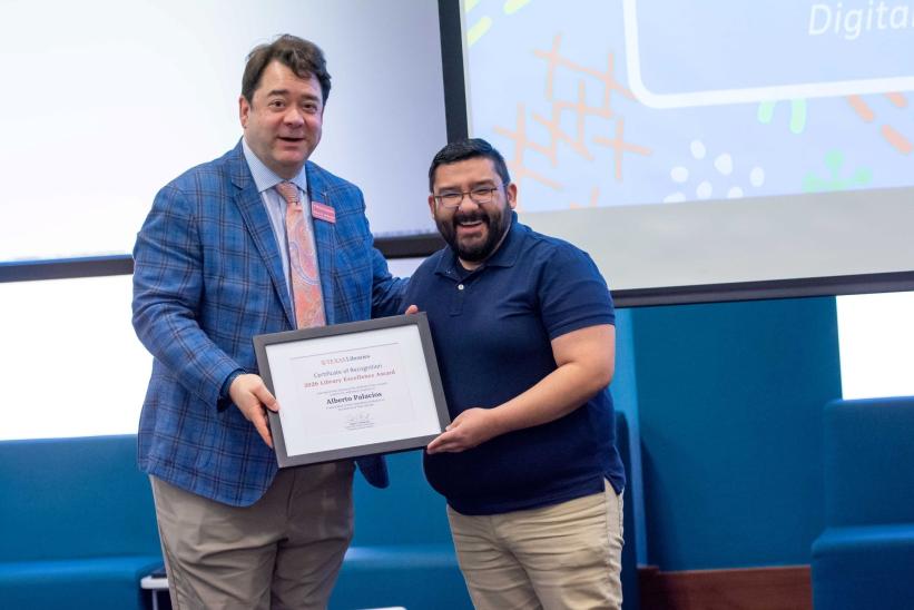 Man in blue polo receives framed Library Excellence Award