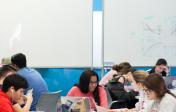 groups of students collaborating at tables around whiteboards