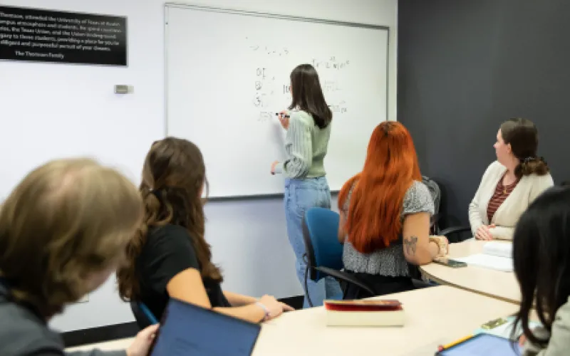 A group of students using a study room one of them is writing on the white board while the others watch